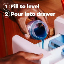 Liquid laundry detergent bottle, orange with blue cap, pouring into washer detergent drawer