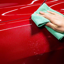 Hand wiping a car hood with a green microfiber cloth