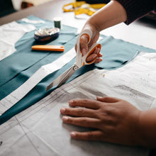 Hands using white-and-orange fabric scissors on blue patterned cloth