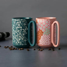 Two stoneware mugs with teal and pink butterfly flower prints and curved handles