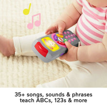 Baby hands gripping a gray learning remote toy with a red top and colorful buttons