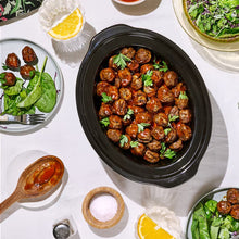 Slow cooker insert filled with glazed meatballs and herbs