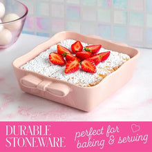 Pink square ceramic baking dish with bow-shaped handles, filled with powdered cake and strawberries