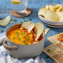 Potato chips with a bowl of dip and extra chips in white bowls