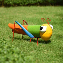 Metal grasshopper yard stake with yellow head, green body, blue stripe, orange wings, red wire legs