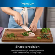 Stainless steel chef knife slicing herbs on a wooden cutting board
