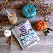 Organic pumpkin seed protein powder pouch on table with drink cup and small pumpkin