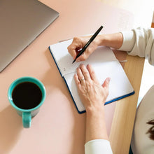 Coffee mug with dark coffee beside an open notebook and pen on desk
