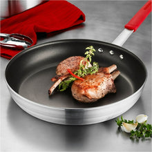 Nonstick small frying pan with black interior, red handle, and cooked cutlets with herbs.