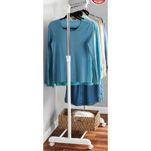 Rolling clothes rack with hanging shirts on top bar and storage basket on the base
