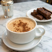 Cup of coffee with frothy top and saucer, with dark biscuits on side plate