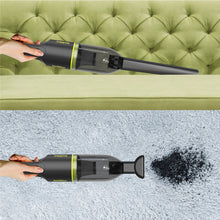 Handheld cordless vacuum in green with clear dust cup, used to clean a sofa surface