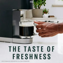 Dark roast coffee mug with foam beside a Keurig machine