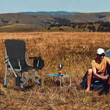 Black folding camping chair with cup holder and side pocket set in grassy field.