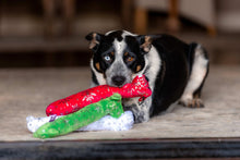 Plush dog loofa toy in red and green with white snowflake print on a floor