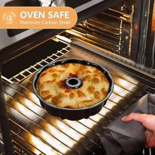 Black bundt cake pan on an oven rack with cake inside.