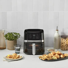 Black basket air fryer with digital top display and silver handle, shown with prepared food trays