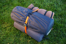 Orange tie-down strap with cam buckle securing a rolled bag