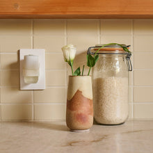Wall plug-in diffuser with two glass jars and flower stems on a kitchen counter