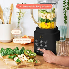 Black blender with clear jar and chopped fruit and vegetables on cutting board