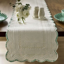 Quilted white table runner with green edging and scalloped border; stitched decorative panel