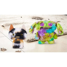Calico cat plush with jagged teeth and yellow eyes beside a colorful monster toy