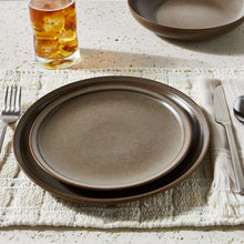 Brown stoneware dinner plate with speckled glaze, set on table with drink and utensils