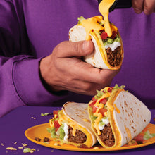 Hand-held tacos with melted queso drizzle over a saucy filling
