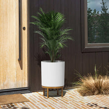 Capri planter with wood stand, white ribbed pot with palm fronds on porch
