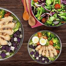 Stainless steel mixing bowls filled with salad ingredients and herbs