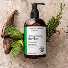 Strengthening shampoo bottle with pump and rosemary mint sprigs on stone.