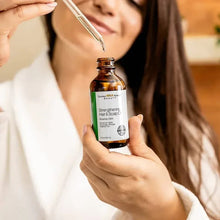Hair and scalp oil bottle with dropper being held, amber glass and black cap