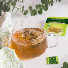 Green tea in clear glass mug with pouring stream and Bigelow tea packets