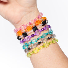 Hand wearing stacked beaded bracelets in pink, orange, purple, teal, clear, black, and green