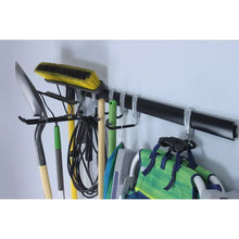 Wall utility storage rail with staggered hooks holding brooms, tools, and gloves