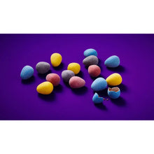 Colorful candy mini eggs in blue, yellow, purple, and pink on a dark surface