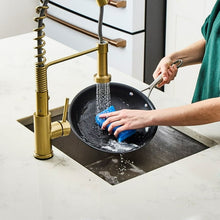 Black non-stick fry pan being scrubbed with a blue sponge and metal tool