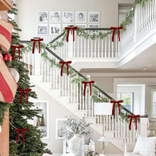 Set of red velvet Christmas bows tied along a staircase garland and railing.