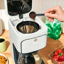 White coffee maker brewing basket with dark grounds and hand placing a scoop