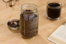 Wide-mouth glass mason jar with metal lid, filled with dark coffee beans