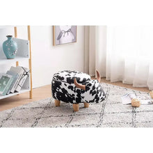 Cow-print ottoman with rounded seat, brown horns, and short wooden legs