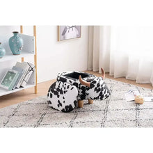 Cow-print ottoman with rounded cushion, brown horns, and short wooden legs