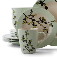 Green stoneware dinner plate with floral branch motif and stack of bowls and mug behind