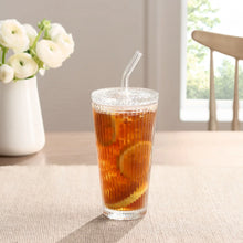Ribbed glass tumbler with amber iced drink, glass lid, and straw