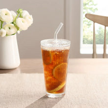 Ribbed glass tumbler with glass lid and clear straw filled with iced tea.