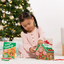 Child decorating a wooden gingerbread house play set with red icing pieces