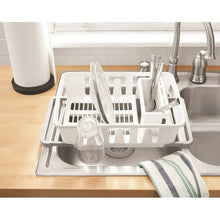 White dish drying rack with utensil holder holding cups on countertop near sink