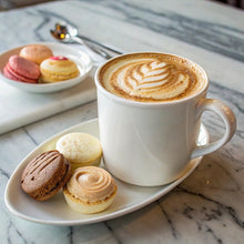 White coffee cup with light-brown crema foam and saucer with pastries