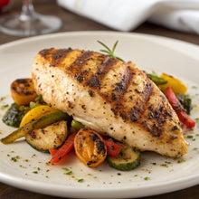 Grilled chicken breast with visible lemon pepper seasoning and colorful vegetables on a plate