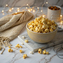 Butter popcorn in a ceramic bowl with scattered popcorn pieces on a tray